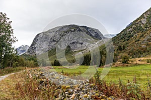 Countryside in green norway mountains landscape. Bright colors natural summer cloudy view. Red green fields, stones and pine