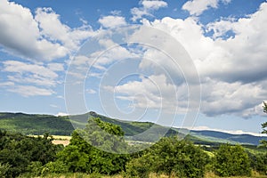 Countryside at high noon. Rural scenery with trees and fields on the rolling hills at the foot of the ridge