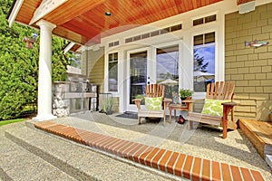 Countryside house exterior. View of column porch with chairs and concrete floor.