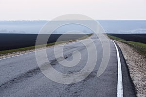 Countryside landscape minimalist style. Empty eneven asphalt road with white road marking in empty black fields in early morning