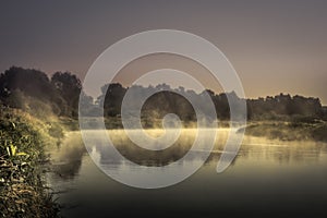 Countryside morning sunrise river mist scenery landscape with tranquil foggy water mirror and dark dramatic moody sky