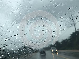 Countryside road view from car`s front windscreen which focus on raindrops