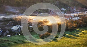 Countryside rural landscape with village over sunbeam in misty morning