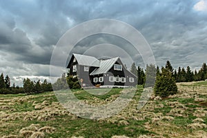 Countryside scene with wooden house and cloudy sky on background. Farm house surrounded by trees and fields.Lonely tourist house