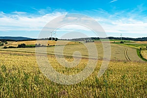 Countryside scenery with yellow and green wheat fields, hills and wind energy generator turbines