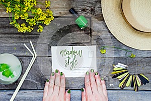 Countryside travel and vacation background. Female hands holding postcard surrounded with glass of lemonade, straw hat, wildflower