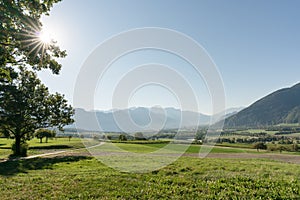 Countryside view with sun shining and fields and forest and mountains in early autumn