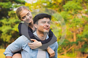 Coupe in park. Boyfriend carrying his girlfriend on piggyback