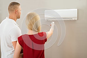 Couple Adjusting Temperature Of Air Conditioner