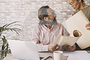 Couple of adult business colleagues working together at the desk with laptop and big paper design. People and office home