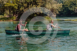 Couple adventurous explorer friends are canoeing in a wild river surrounded by the beautiful nature