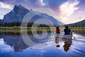 Couple adventurous friends are canoeing in a lake surrounded by the Canadian Mountains.