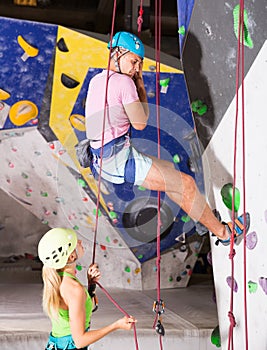 Couple of alpinist practicing in pair indoor rock-climbing