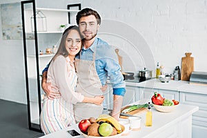 couple in aprons hugging and looking at camera