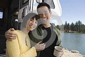 Couple with arms around each other outside RV at lake