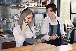 Couple asian barista owner coffee shop standing at counter welcome the customer. Cheerful two young barista man and woman in apron