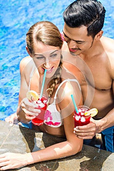 Couple in Asian hotel pool drinking cocktails