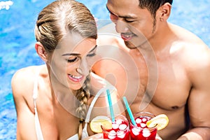 Couple in Asian hotel pool drinking cocktails