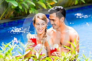 Couple in Asian hotel pool drinking cocktails