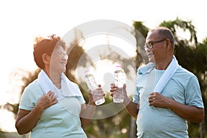 A couple of asian old man and woman doing physical exercise outdoor and holding plastic bottle drinking water. Be healthy and