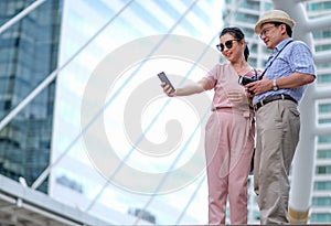 Couple of Asian old man and woman tourist are acting of selfie photo capture among the big building of big city. This photo also