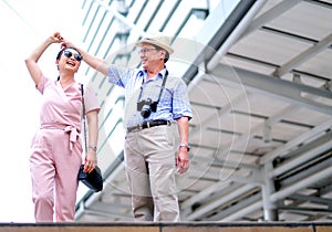 Couple of Asian old man and woman tourist are dancing among the big building of big city. This photo also contain concept of good