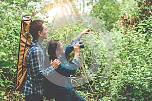 Couple of Asian people holding binoculars telescope in forest looking forward to destination. People lifestyles and leisure