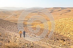 Couple backpackers walking ascending hill Negev desert, Israel.