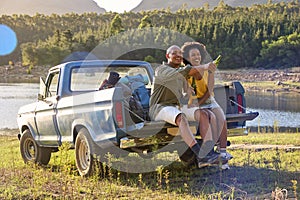 Couple With Backpacks In Pick Up Truck On Road Trip By Lake Drinking Beer