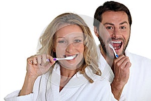 Couple in bathrobes cleaning teeth