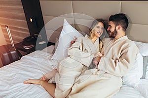 Couple in bathrobes lying on bed in hotel room