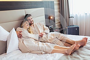 Couple in bathrobes lying on bed in hotel room