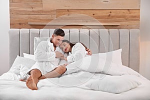Couple in bathrobes resting on bed at home