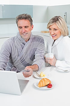 Couple in bathrobes using laptop in kitchen