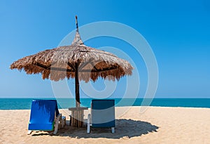 Couple beach chairs and umbrella on tropical beach with sea and blue sky background.