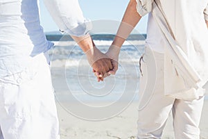 Couple on the beach looking out to sea holding hands