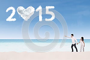 Couple on beach pointing at number 2015