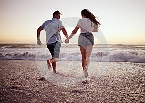 Couple, beach and running, holding hands in waves at sunset on romantic holiday. Love, freedom and a man and woman on