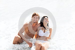 Couple on beach, sitting in water wave foam sea