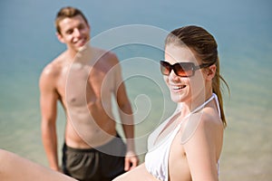 Couple on beach - sunbathing in swimsuit by sea