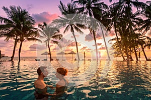 Couple at beach vacation holidays resort relaxing in swimming pool with scenic tropical landscape at sunset, romantic summer