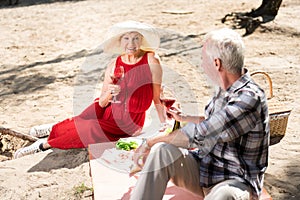 Couple of beaming pensioners drinking wine and eating salad during picnic