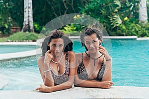 Couple of beautiful sexy women in leopard swimsuits relaxing near swimming pool, posing and tanned on summer vacation