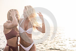 Couple of beautiful slim fitness babes in friendship and relationship at the sea with sunset in backlight for background.