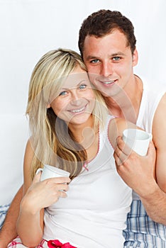 Couple in bed drinking coffee and smiling