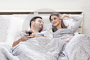 Couple in bed with electronic devices in morning