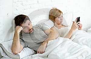 Couple in bed husband frustrated upset and unsatisfied while his internet addict wife is using mobile phone