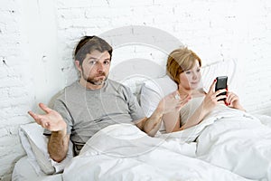 Couple in bed husband frustrated upset and unsatisfied while his internet addict wife is using mobile phone