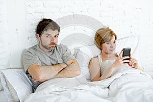 Couple in bed husband frustrated upset and unsatisfied while his internet addict wife is using mobile phone