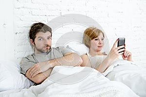 Couple in bed husband frustrated upset and unsatisfied while his internet addict wife is using mobile phone